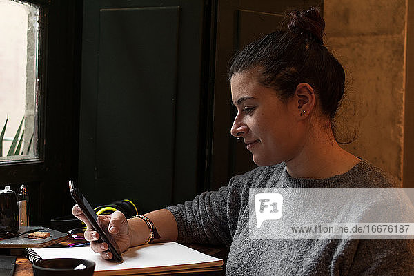 Young woman looks at her phone while studying in a retro pub