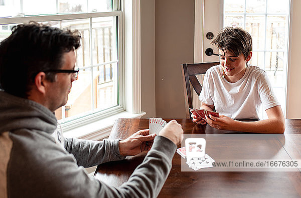 Heranwachsender Junge und sein Vater spielen gemeinsam Karten am Tisch.