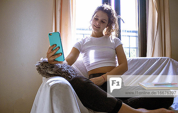 Frau macht ein Selfie auf einem weißen Sofa vor dem Fenster