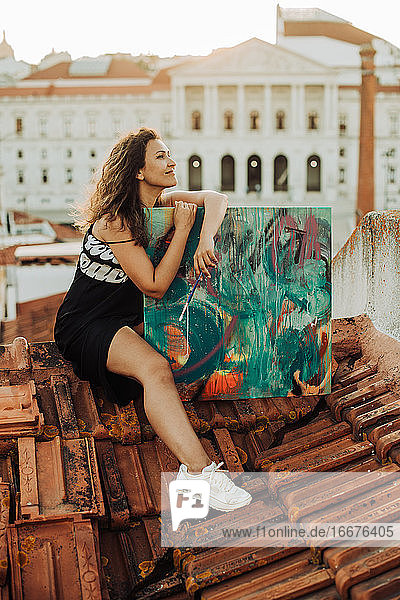 Eine Malerin sitzt mit ihrem Kunstwerk auf einem Ziegeldach