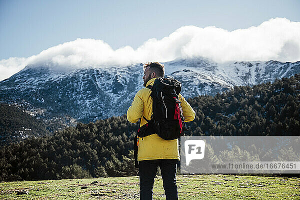 Junger Mann mit gelber Jacke und Rucksack in den Bergen.