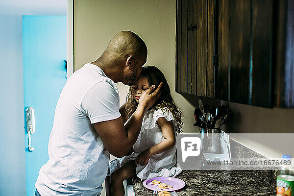 Vater küsst Tochter  während sie auf dem Küchentisch sitzt