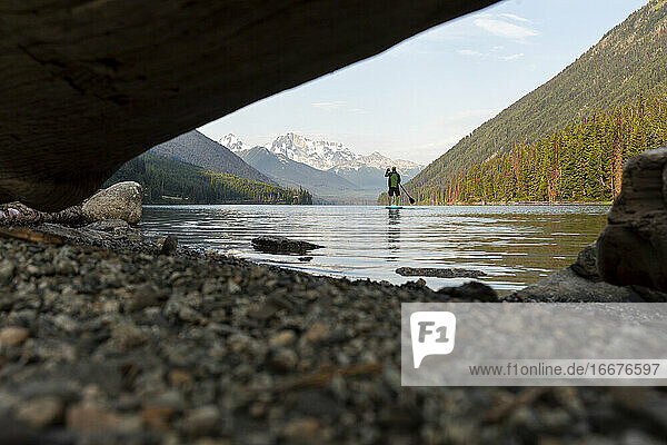 Anonymous traveler on paddle board on calm mountain lake at sunrise