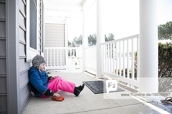 Wide View of Boy in Pink Snow Pants Sitting on Snowy Front Porch
