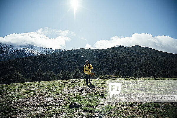 Junger Mann mit gelber Jacke und Rucksack in den Bergen.