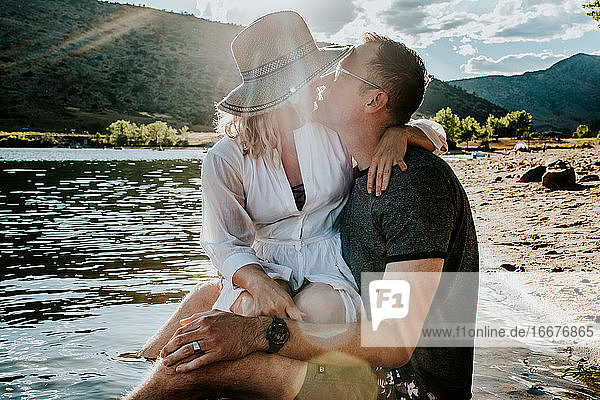 Mann und Frau sitzen zusammen und küssen sich am Seeufer