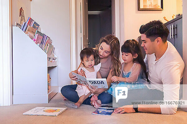 Family of four sitting on the floor and reading children's books.