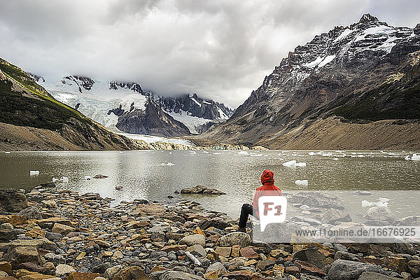 Rear view of young man in red jacket sitting by Laguna Torre  Los Glaciares National Park  El Chalten  Patagonia  Argentina