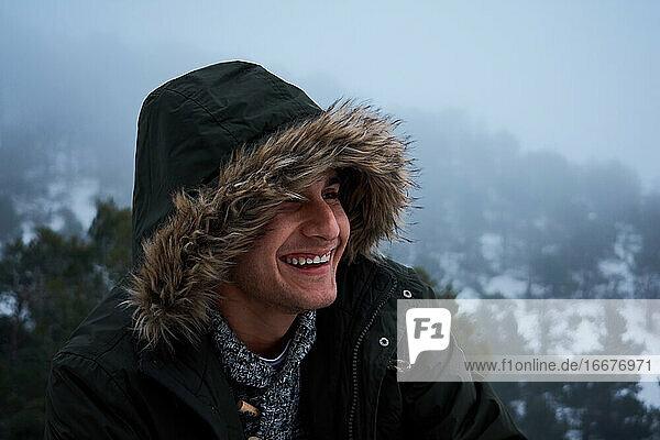 Lateinischer junger Mann lächelt in einem Mantel an einem verschneiten Tag