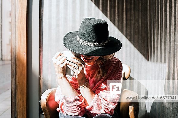Frau saß versteckt hinter einem Hut und trank Kaffee in einem Café im Herbst