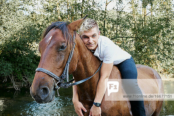 Porträt eines jungen blonden Mannes  der auf einem Pferd über einen Fluss reitet