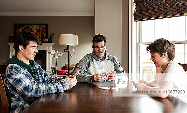 Vater und heranwachsende Söhne spielen gemeinsam Karten am Tisch.