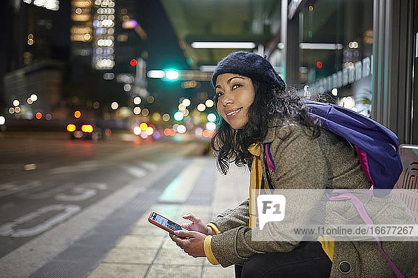 lächelnde Frau  die nachts auf dem Busbahnhof sitzt