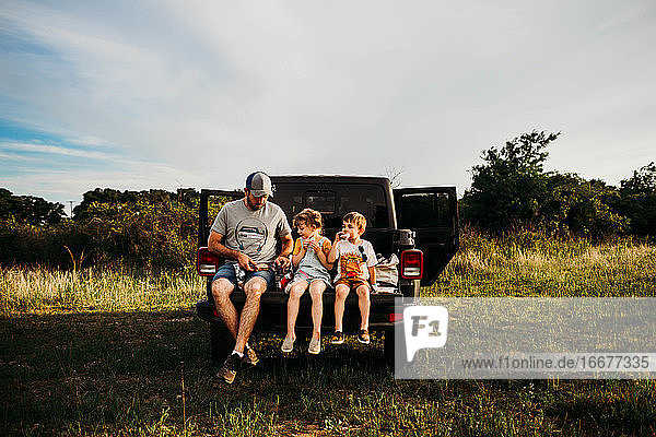 Papa und zwei Kinder machen ein Picknick auf der Heckklappe eines Lastwagens