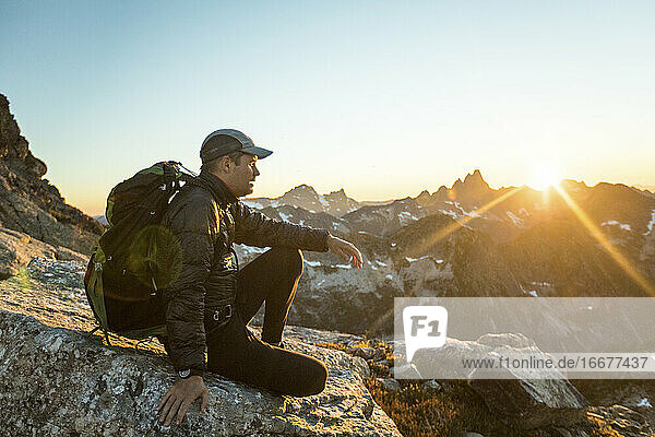Rucksacktourist sitzt auf einem Berggipfel und genießt den Blick auf den Sonnenuntergang.