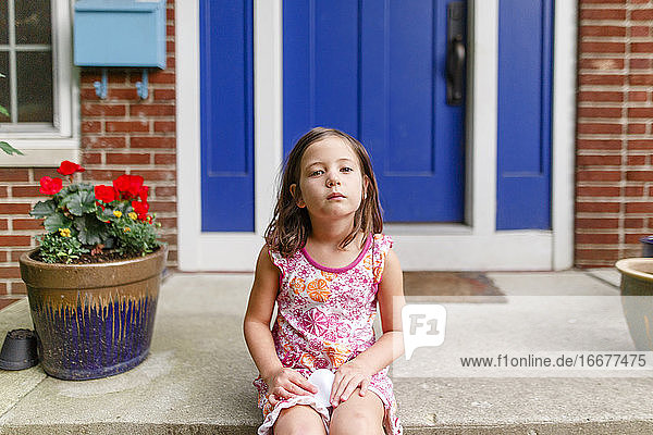 Ein kleines Kind sitzt mit ernster Miene auf der Treppe vor seinem Haus