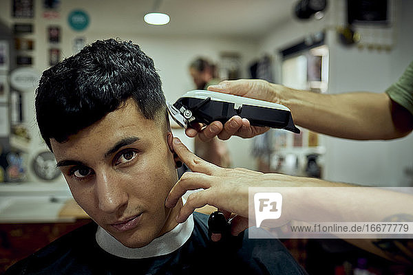 Ein Junge schaut in die Kamera  während er sich die Haare maschinell schneiden lässt
