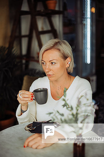 Blonde osteuropäische Frau trinkt Kaffee und sitzt am Tisch