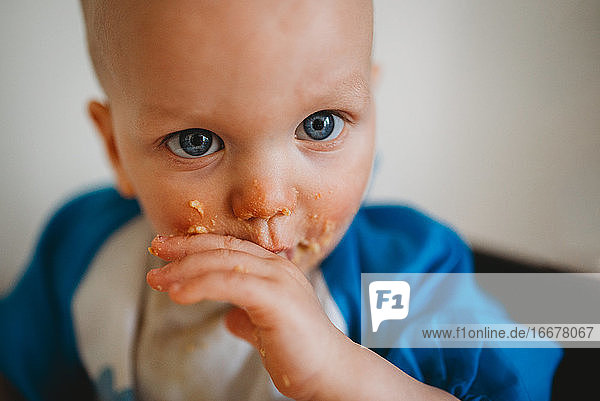 Nahaufnahme eines schönen Babys mit blauen Augen  das mit seinen Händen isst
