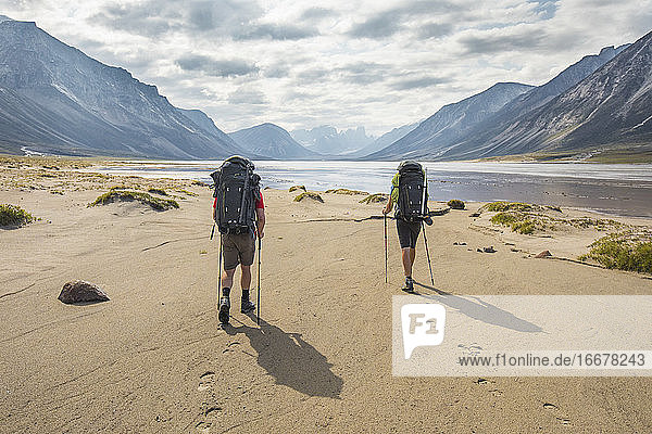 Rear view of two backpackers hiking  leaving footprints in the sand.