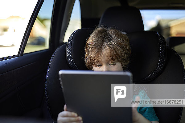 Boy using digital tablet while traveling in car