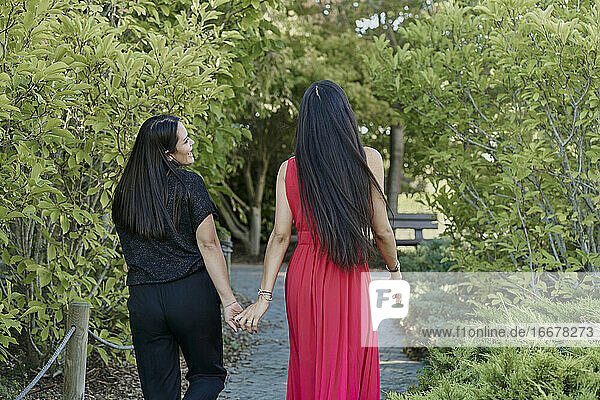 Junge Frauen Paar hält die Hände zu Fuß auf grünem Gras in einem Park an einem sonnigen Tag. romantisches Konzept