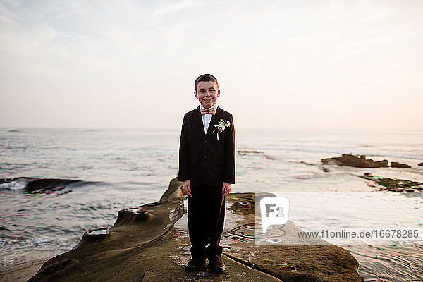 Neunjähriger Junge im Smoking auf einem Felsen am Strand von San Diego stehend