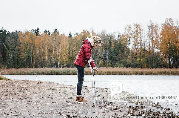 injured woman stood at the beach with crutches looking thoughtful