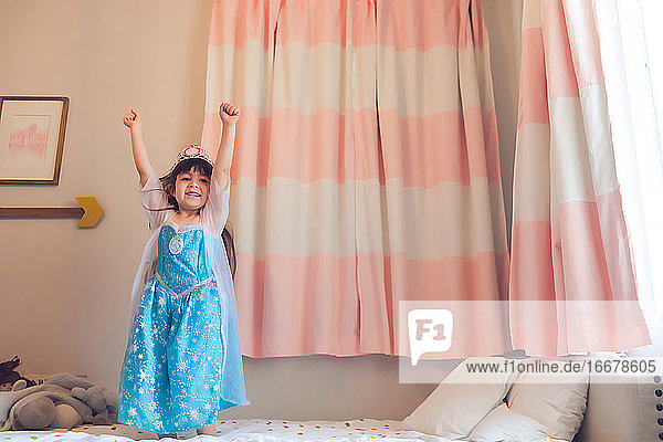 Kleines Mädchen  verkleidet als Prinzessin  die auf ihrem Bett hüpft.