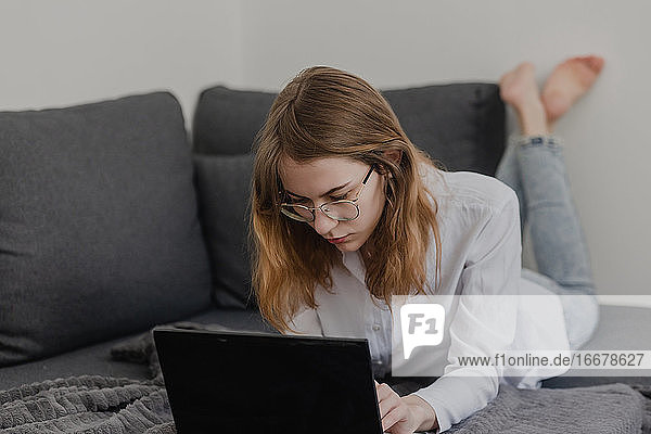 Attraktive junge Frau  die von zu Hause aus arbeitet - Unternehmerin  die auf dem Sofa mit einem Laptop sitzt und ihr Handy von zu Hause aus überprüft