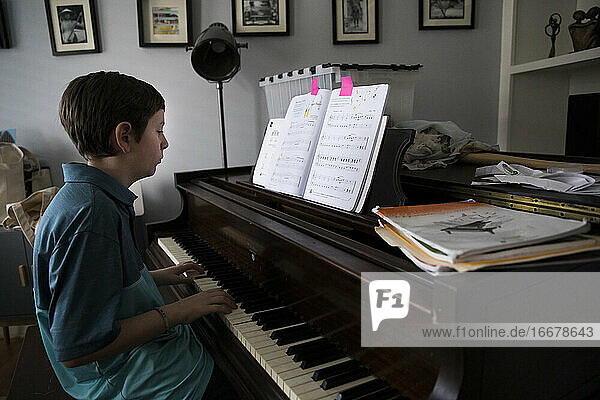 Seitenansicht eines Teenagers  der zu Hause Klavier spielt  mit markierten Seiten im Buch