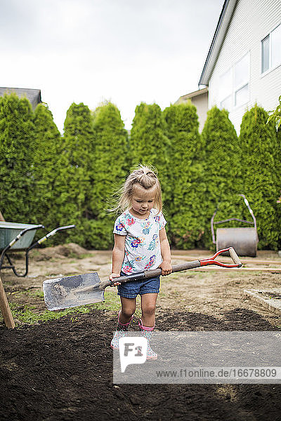 Nettes Mädchen hält eine Schaufel und gräbt im Hinterhof ihres Hauses.