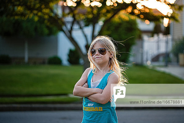 Porträt eines blonden jungen Mädchens  das die Arme verschränkt und eine Sonnenbrille trägt