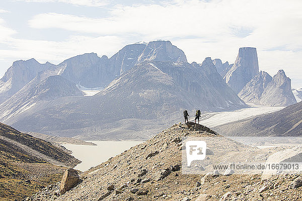 Two hikers stand on high mountain ridge in Akshayak Pass Baffin Island