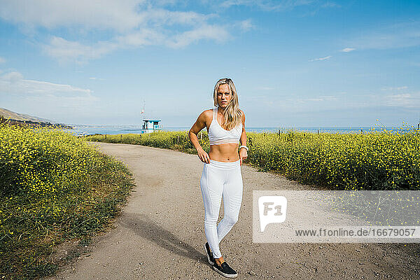 Junge Frau auf unbefestigtem Weg zum Strand  umgeben von gelben Wildblumen