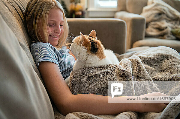 Junges Mädchen rollt sich auf dem Sofa zusammen und betrachtet eine weiße Katze