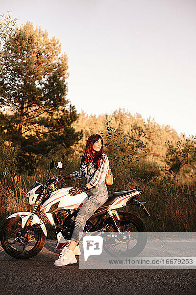 Junge Frau  die auf einem Motorrad auf einer Landstraße sitzt und zurückblickt