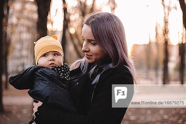 Glückliche junge Mutter mit ihrem kleinen Sohn im Herbst im Park stehend