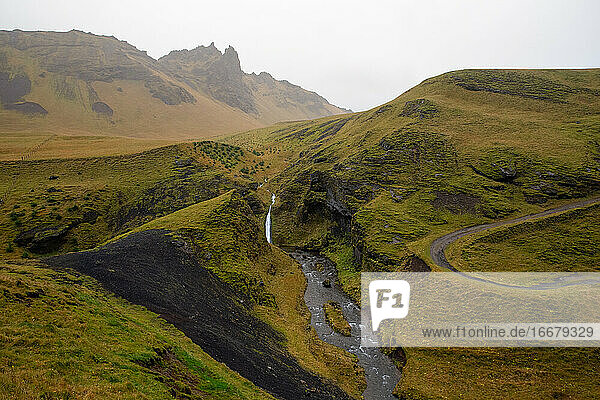 Ein Strom durchschneidet die grünen  moosbewachsenen Hügel in Island
