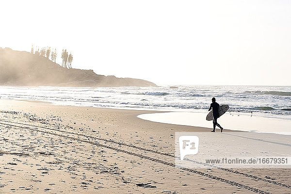 Unbekannter Mann läuft mit Surfbrett am Strand