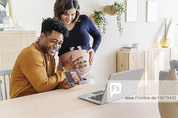 Ehemann und schwangere Frau sehen sich Ultraschallbilder ihres Babys an. Unter