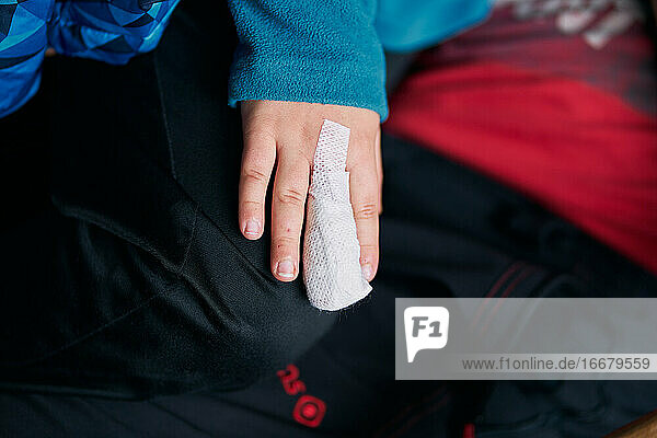 Unkenntlich gemachtes Kind  das einen bandagierten Finger zeigt  während es in den Armen eines Elternteils sitzt