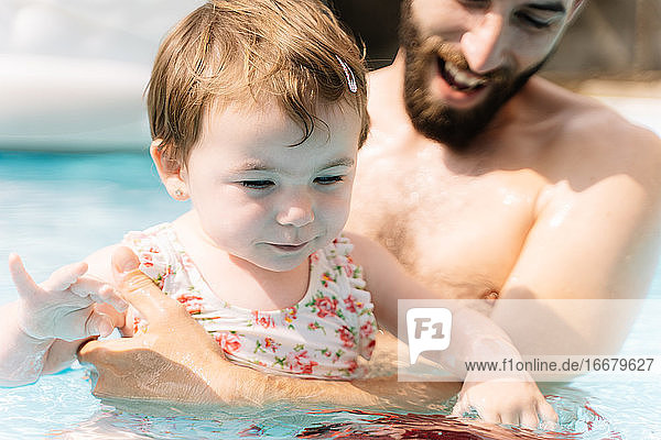 Selective focus on the face of a girl in a flower bathing suit in the water embracing a man