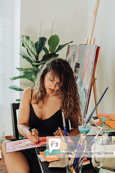 Eine Malerin  die an einem Tisch in ihrem Atelier sitzt und sich auf ihre Arbeit konzentriert