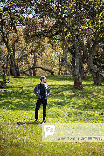 Full body portrait of young man casually dressed outdoors with trees