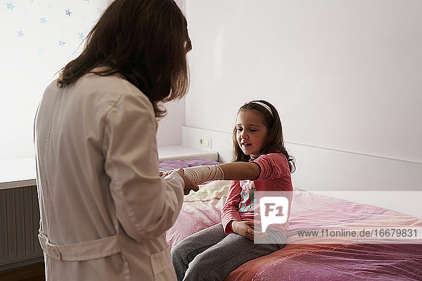 Ärztin bandagiert den Arm eines kleinen Mädchens in ihrem Zimmer. Hausarzt Konzept