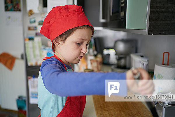 Mädchen mit roter Kochmütze steht in der Küche ihres Hauses