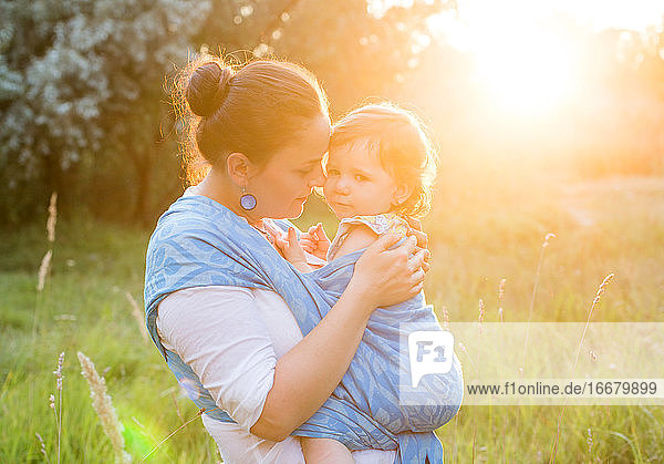 Mother and wrapped daugher in sling  carrier in sun light