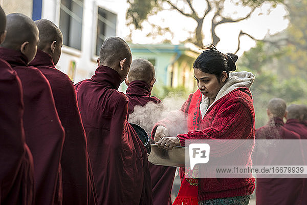 Eine burmesische Frau gibt gedämpften Reis an Mönche  die in der Schlange stehen  Nyaung U  Myanmar