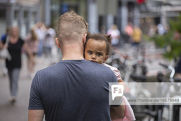 A young dad carrying his mixed race daughter in the city